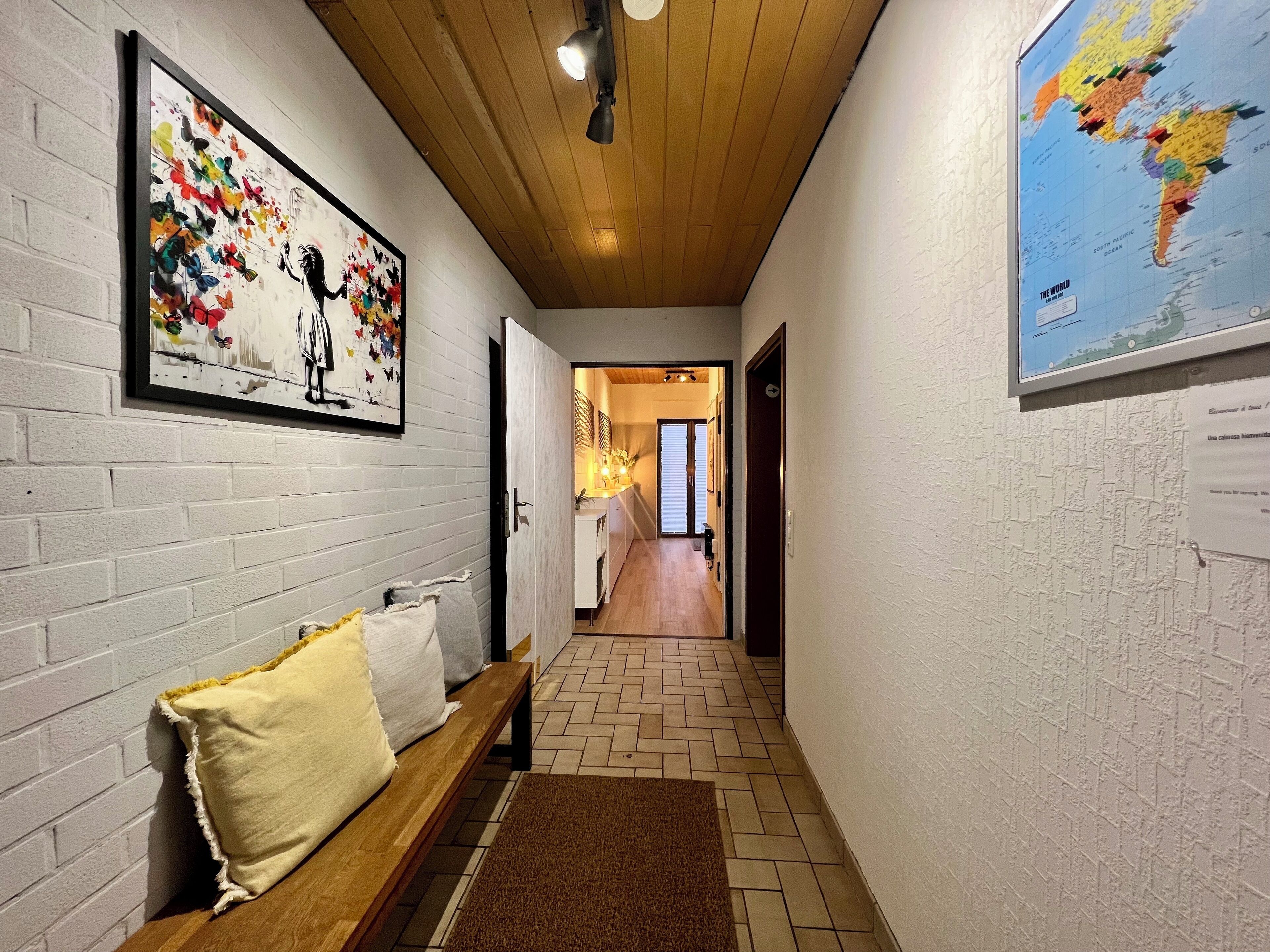 Ein Flur mit einer hölzernen Bank, einem gerahmten Schmetterlingsbild, einer Karte an der Wand und einem Fliesenboden.