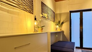Una camera da letto compatta con un letto, un piccolo ripiano con piante, una lampada fissata al muro e una porta scorrevole su un balcone.