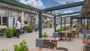 An outdoor café area with tables and chairs, a man standing near a sign, and a covered walkway. - Nice apartment in Großenbrode OT Lütjenb with WiFi (Großenbrode OT Lütjenb)
