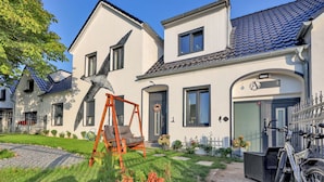 A two-story house with a swing set in the front yard, a bicycle parked outside, and a clear blue sky. - Nice apartment in Großenbrode OT Lütjenb with WiFi (Großenbrode OT Lütjenb)