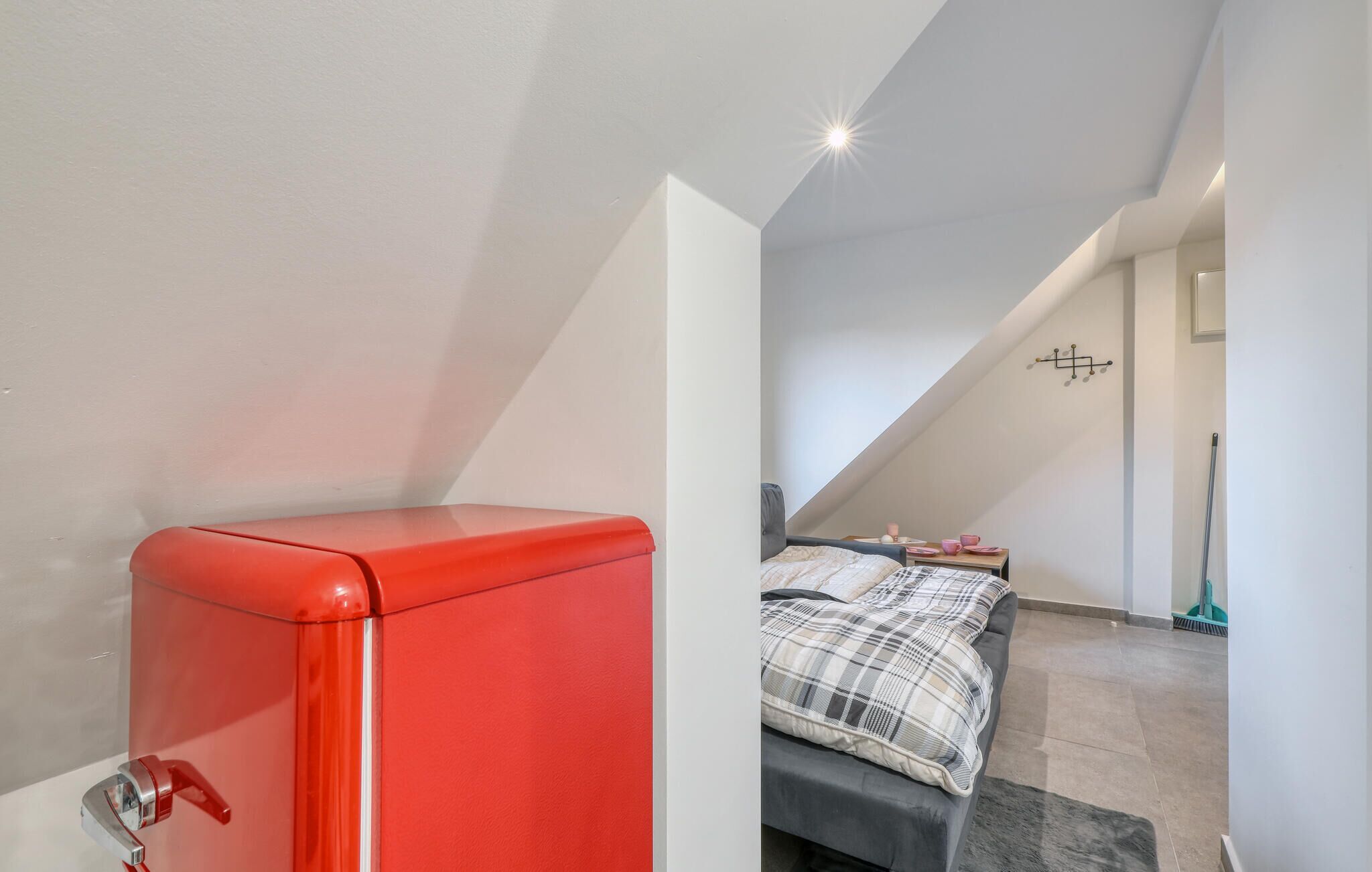 Een compacte kamer met een rode kast, een bed met een geruit plaid en een plafondlamp.