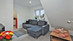 A modern living room with a grey sectional sofa, a wooden coffee table, and a view of the outdoors through a window. - Nice apartment in Großenbrode OT Lütjenb with WiFi (Großenbrode OT Lütjenb)
