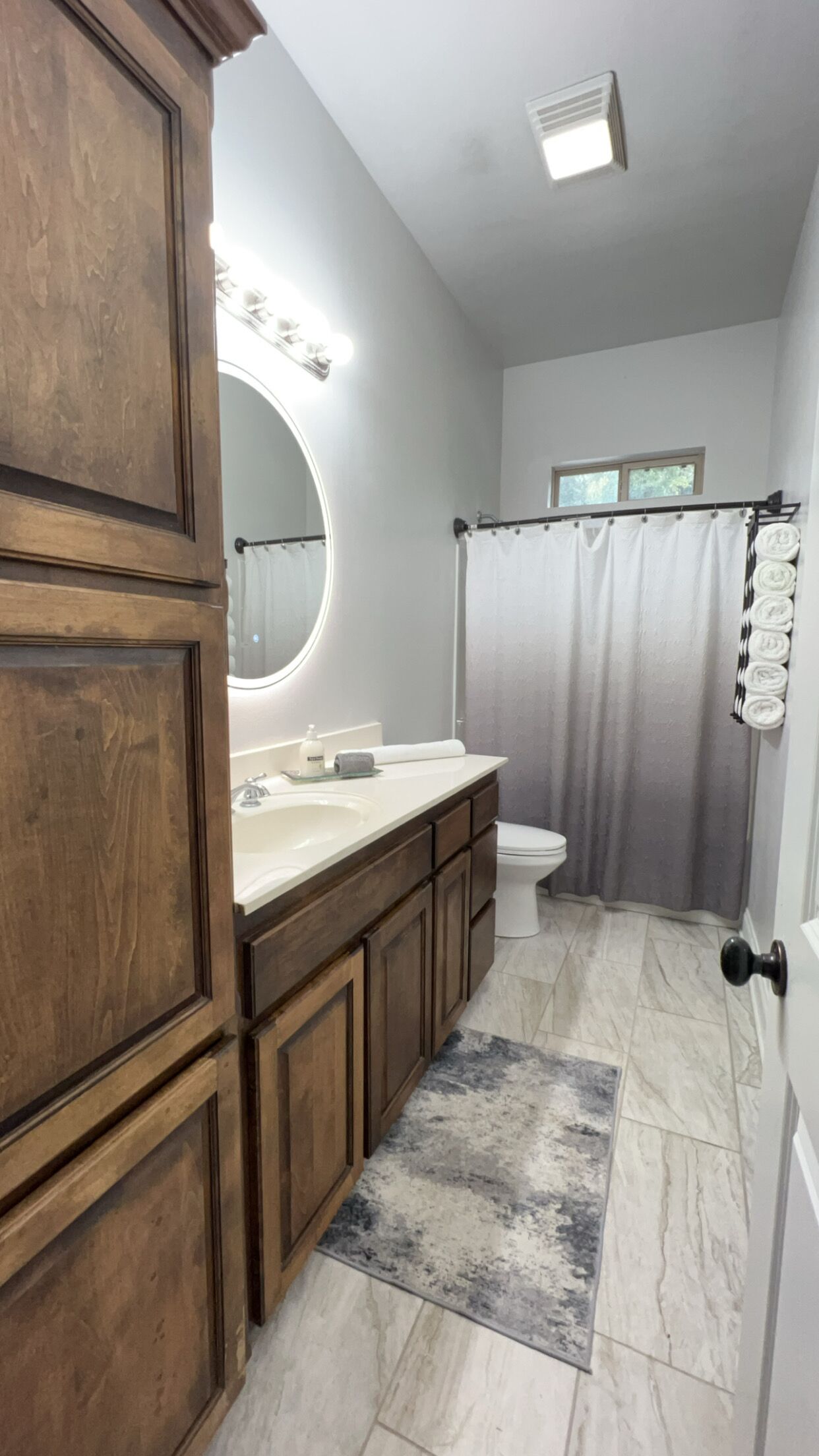 A bathroom with a wooden vanity, a large mirror, a toilet, and a shower curtain.