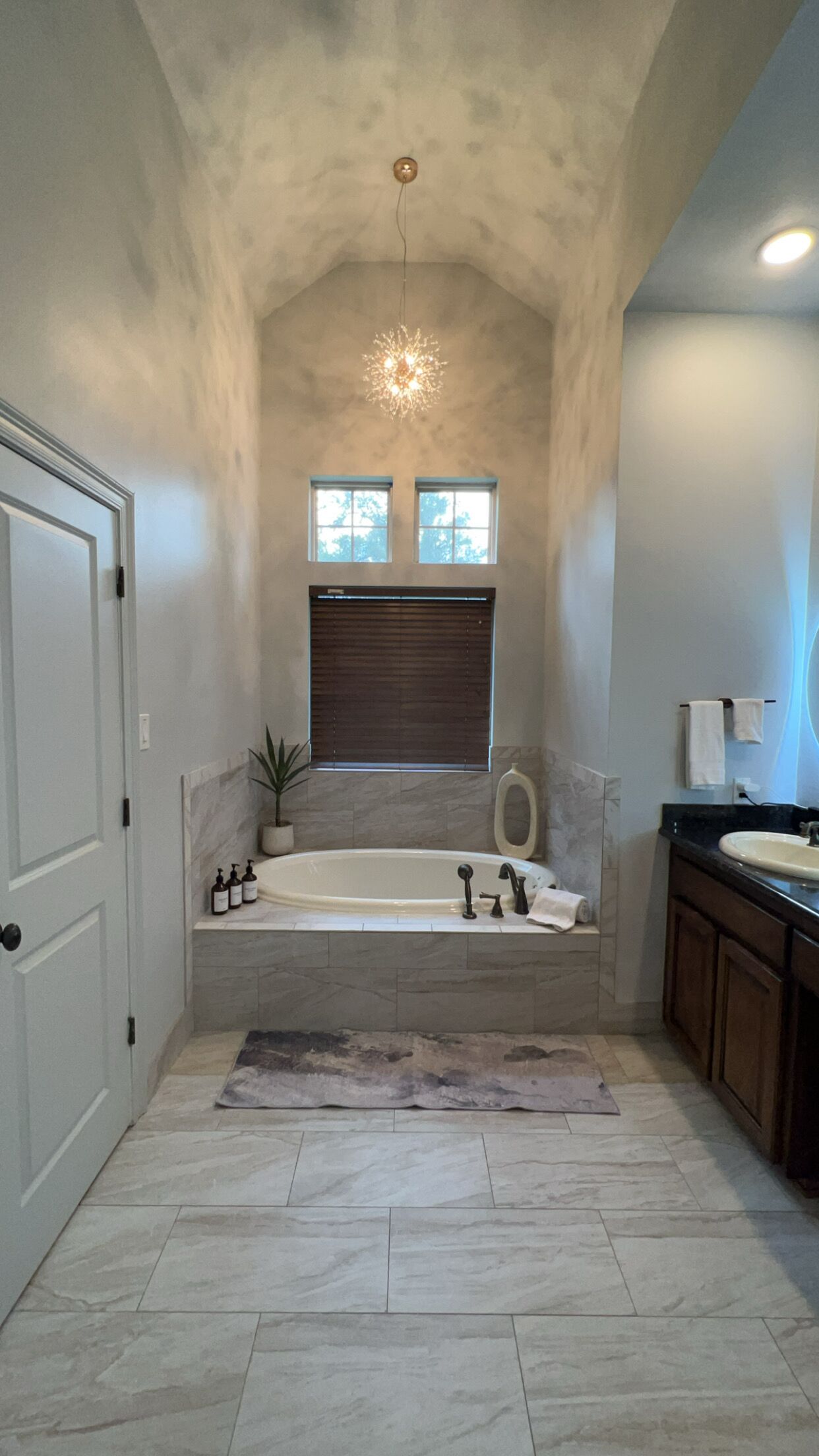 A bathroom with a freestanding bathtub, a window with blinds, a ceiling light fixture, and a sink with a mirror.
