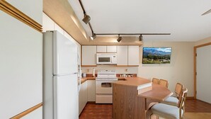 Una cocina compacta con electrodomésticos blancos, una isla de madera y un comedor con sillas.