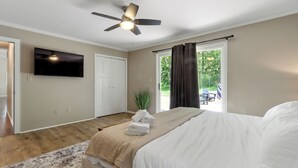 Een slaapkamer met een bed, een plafondventilator, een televisie en uitzicht op het omliggende landschap.