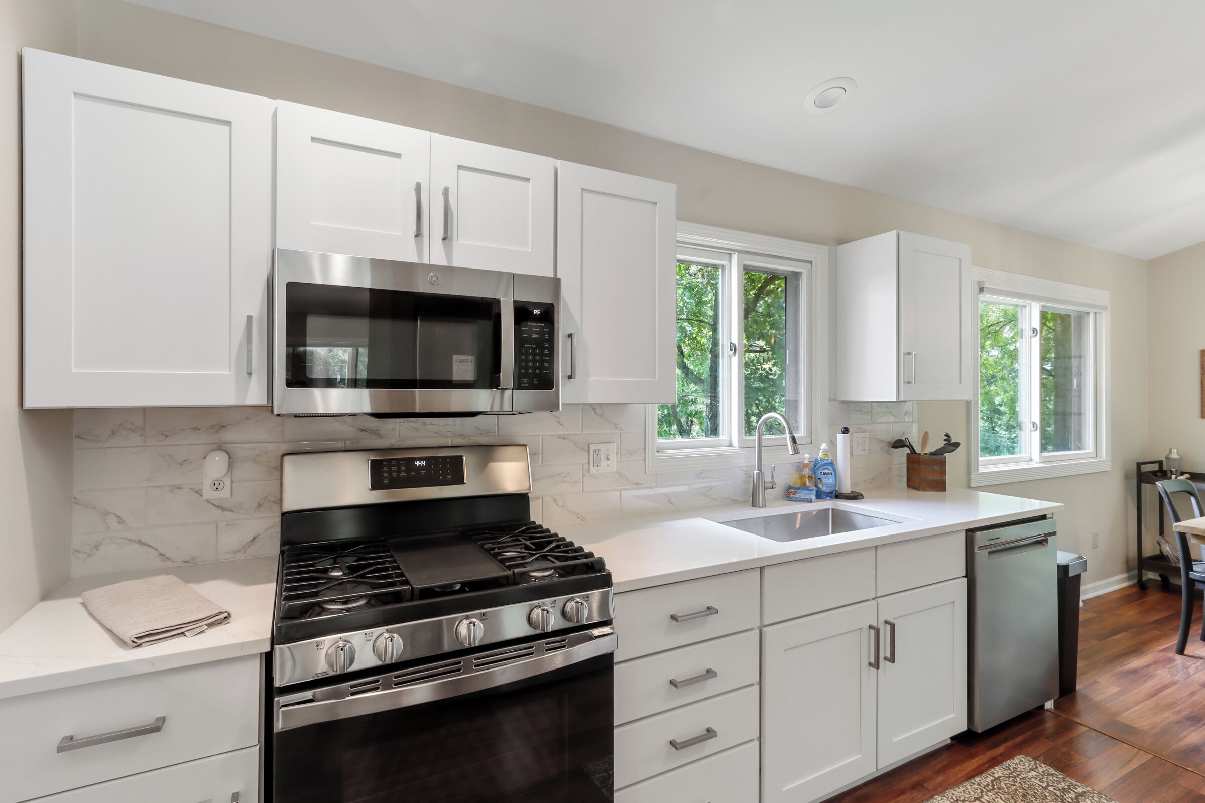 Una cocina moderna con armarios blancos, estufa de acero inoxidable, microondas y lavavajillas.