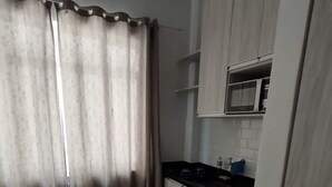 A small, modern kitchen with light wood cabinets, a black countertop, and a microwave.