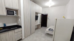 A compact room with a kitchenette, a bed, and a white chair.