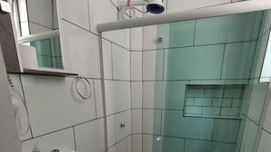 A small, modern bathroom with white tiles, a glass shower enclosure, a white toilet, and a sink with a soap dispenser.