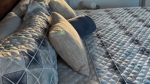 Un dormitorio con una cama grande, un cabecero de madera, una ventana con vistas a un jardín y una mesita con una silla.