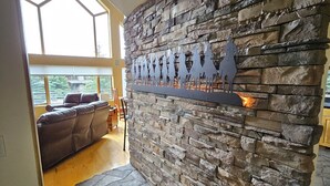 A stone wall with a decorative metal piece, a stone floor, and a view through a large window to the outside. - Charming Big Sky meadows house. Trails and Town Center a short walk away. (Big Sky)