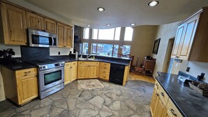 A kitchen with wooden cabinets, a stone floor, and a large window providing natural light. - Charming Big Sky meadows house. Trails and Town Center a short walk away. (Big Sky)
