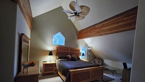 A bedroom with a sloped ceiling, a wooden bed, a nightstand, a lamp, a mirror, and a window with a view of the outdoors. - Charming Big Sky meadows house. Trails and Town Center a short walk away. (Big Sky)