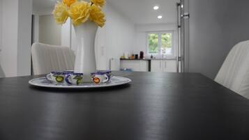 Une table à manger ornée d’un vase de fleurs jaunes, d’une chaise blanche et d’une assiette avec des tasses.