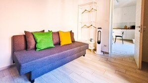 A modern living room with a grey sofa, a glass shelving unit, and a white door leading to a kitchen. - Crispi Penthouse at historic center with panoramic terrace  (Catania)