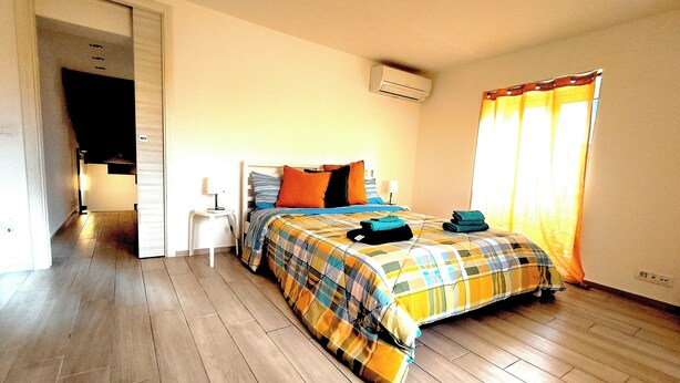 A bedroom with a bed, a nightstand, an air conditioning unit, and a window with curtains. - Crispi Penthouse at historic center with panoramic terrace  (Catania)