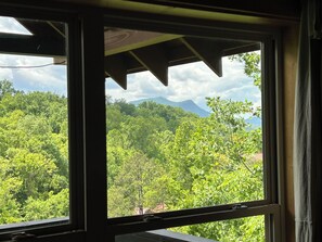 A window with a view of a dense forest and a mountain in the distance. - Mountain View Cabin - Pool, Hot Tub, Theater & Shuffleboard - 1 Mile to Parkway (Pigeon Forge)