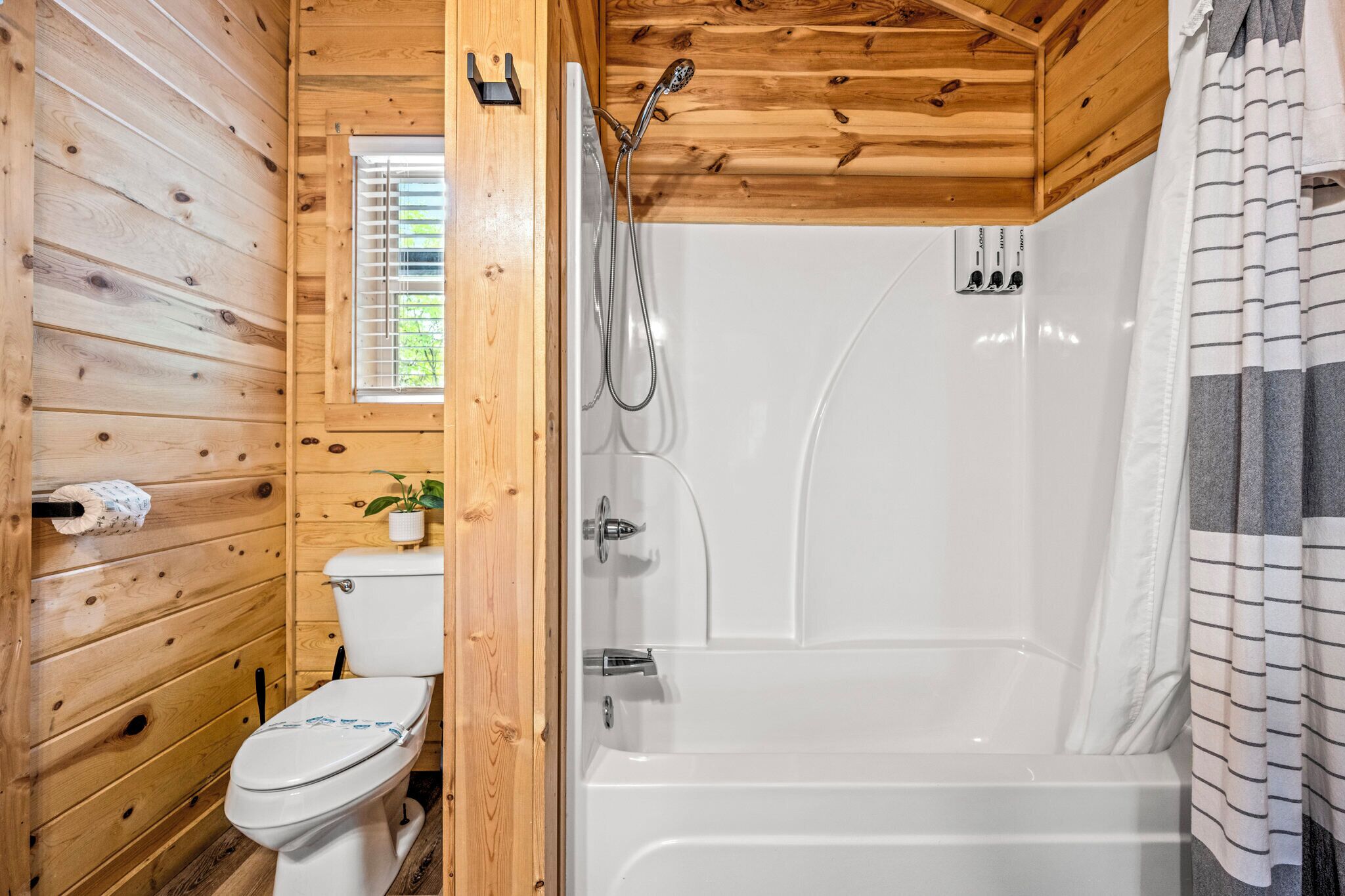 Een houten badkamer in een vakantiehuisje, met een toilet, een douche en een raam.