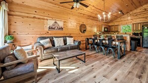 A wooden interior with a sofa, coffee table, dining table, chairs, and a ceiling fan.
