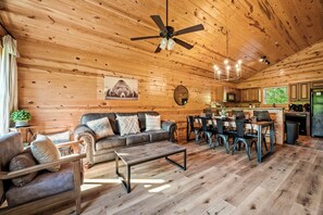 A wooden interior with a sofa, coffee table, dining table, chairs, and a ceiling fan. - Mountain View Cabin - Pool, Hot Tub, Theater & Shuffleboard - 1 Mile to Parkway (Pigeon Forge)