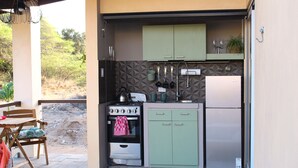 Eine kleine Küche mit Herd, Backofen und Kühlschrank, grünen Schränken und einem Fenster mit Blick auf eine natürliche Landschaft.