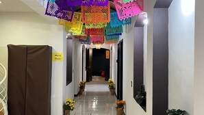 Un pasillo decorado con adornos de papel de colores colgando del techo, plantas en macetas a lo largo de las paredes y un cartel que indica una sala para fines empresariales.
