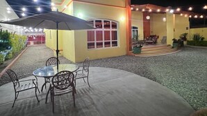 Un espacio al aire libre con patio, una mesa, sillas, luces colgantes y plantas en macetas.