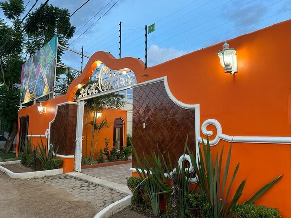 A building with a distinctive orange facade, a decorative entrance gate, and a well-lit pathway leading to the entrance.