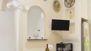 A modern kitchen with a central island, a flat-screen TV mounted above it, and a refrigerator to the right. - Apartment in the heart of Sorrento (Sorrento)