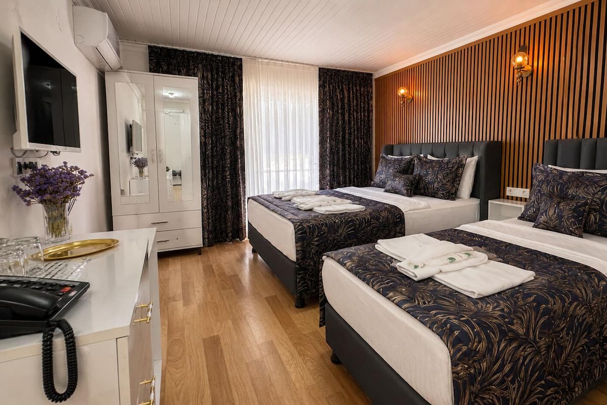 A hotel room with two beds, a desk with a telephone, a mirror, and a wardrobe.