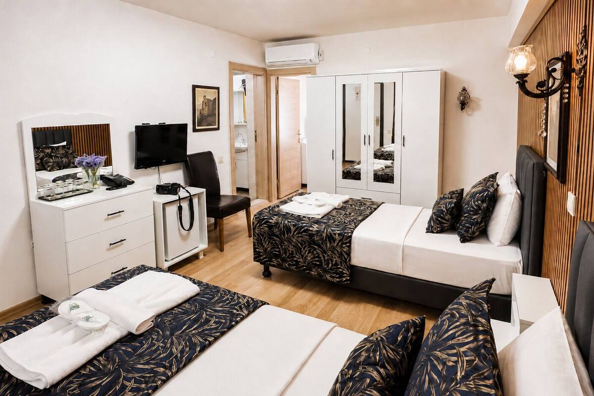 A hotel room with two beds, a desk with a computer, a wardrobe, and a bathroom visible through an open door.