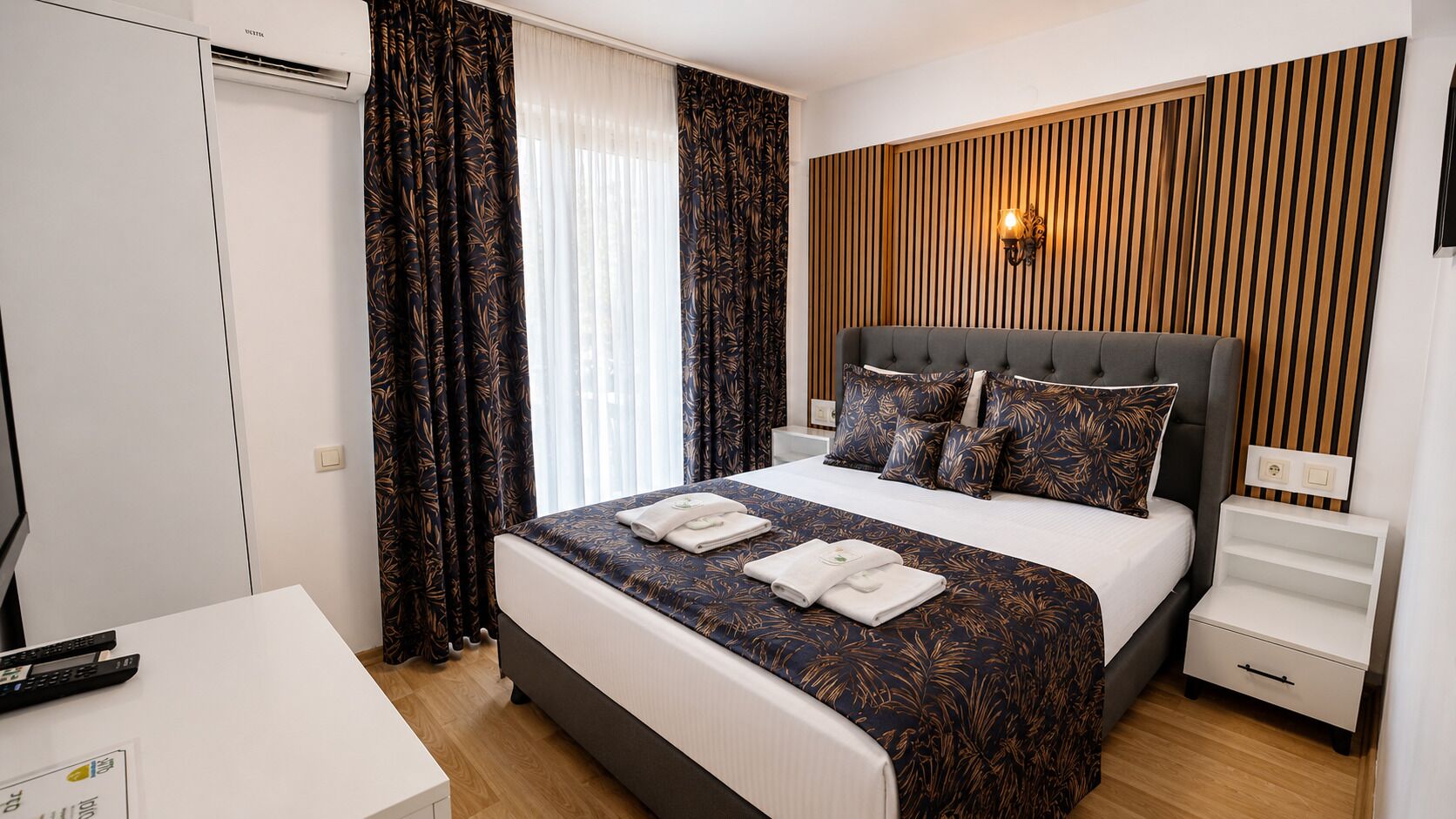 A hotel room with a bed, a nightstand, a TV, and a window with curtains.