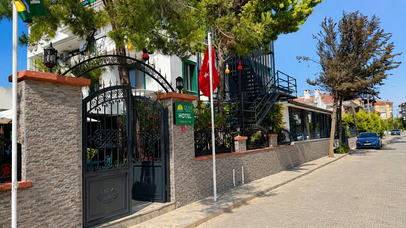 A hotel with a stone facade, a wrought iron gate, and a red flag.