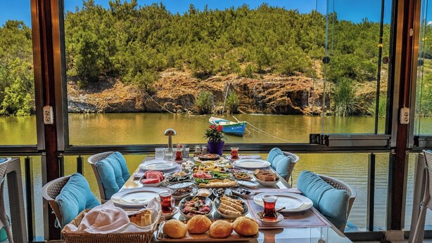 A dining table set with various dishes and a view of a lake with a boat. - Olive Branch Hotel (Ayvalik)