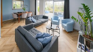 A modern living room with a grey sofa, a blue armchair, and a dining area with a table and chairs.