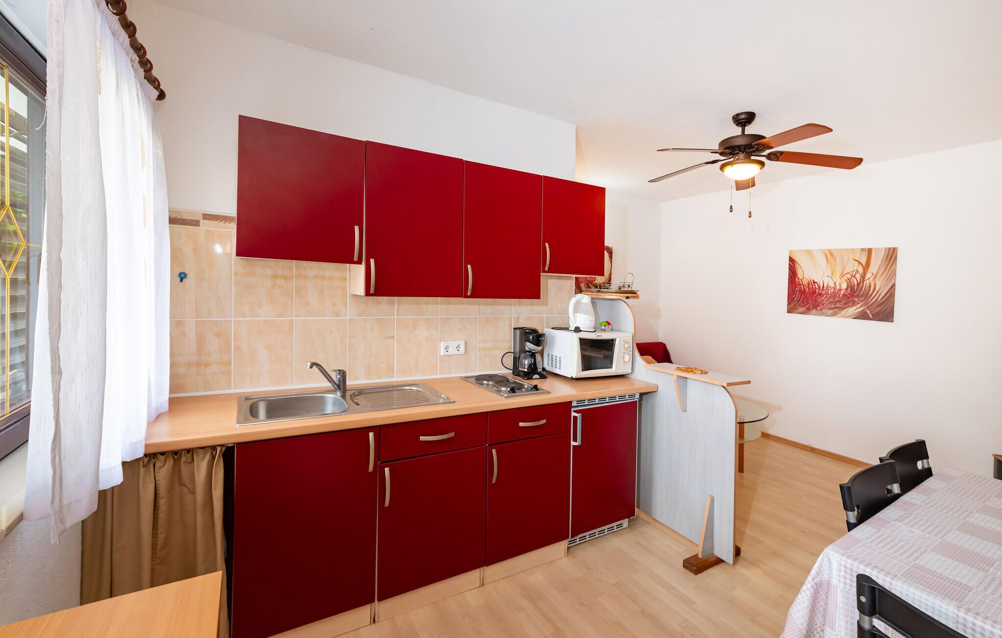 A compact kitchen with red cabinets, a sink, a microwave, and a ceiling fan.