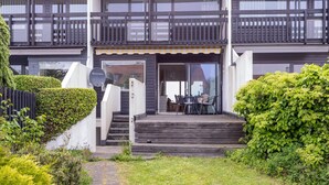 A modern two-story building with a wooden balcony, a covered entrance, and a satellite dish.