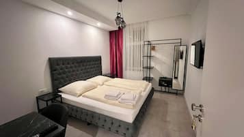 Ein modernes Schlafzimmer mit einem gepolsterten Bett, einem Nachttisch, einem Schreibtisch mit Stuhl, einem Spiegel und einem Kleiderschrank.