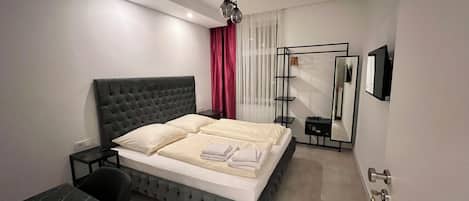 A modern bedroom with a tufted headboard bed, a bedside table, a desk with a chair, a mirror, and a wardrobe.