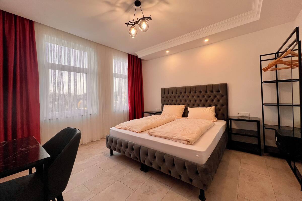 A neatly arranged bedroom with a tufted headboard bed, a small bedside table, and a hanging clothes rack.