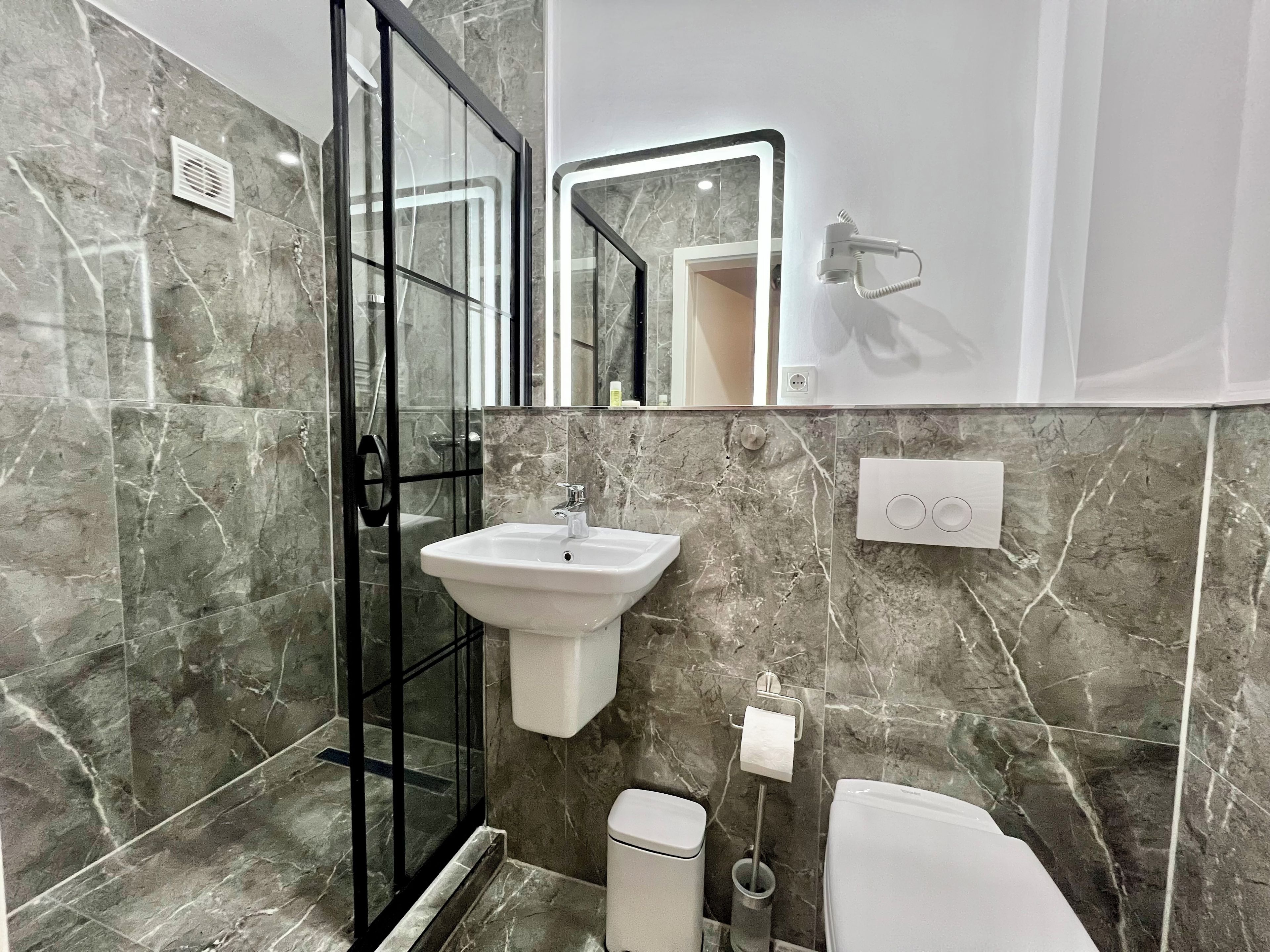 Een badkamer met een douchecabine van glas, een witte wastafel, toilet en een spiegel met verlichting.