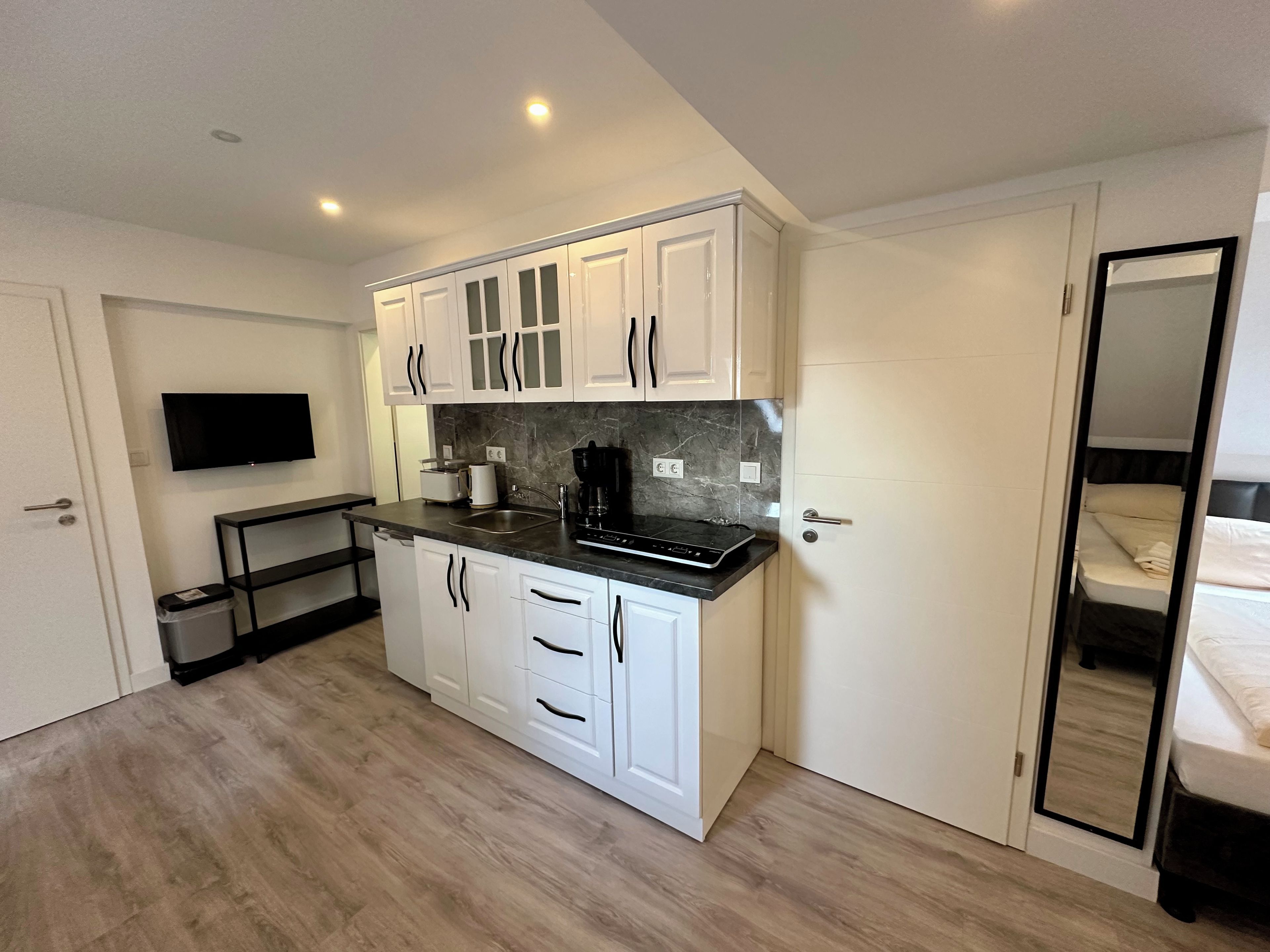 A compact kitchen with white cabinets, a black countertop, a built-in oven, and a TV mounted above the counter.
