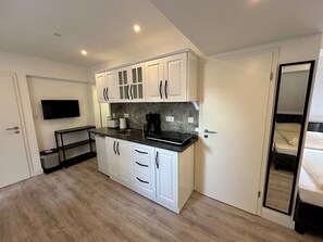 A compact kitchen with white cabinets, a black countertop, a built-in oven, and a TV mounted above the counter. - Durmaz Hotel (Hannover)
