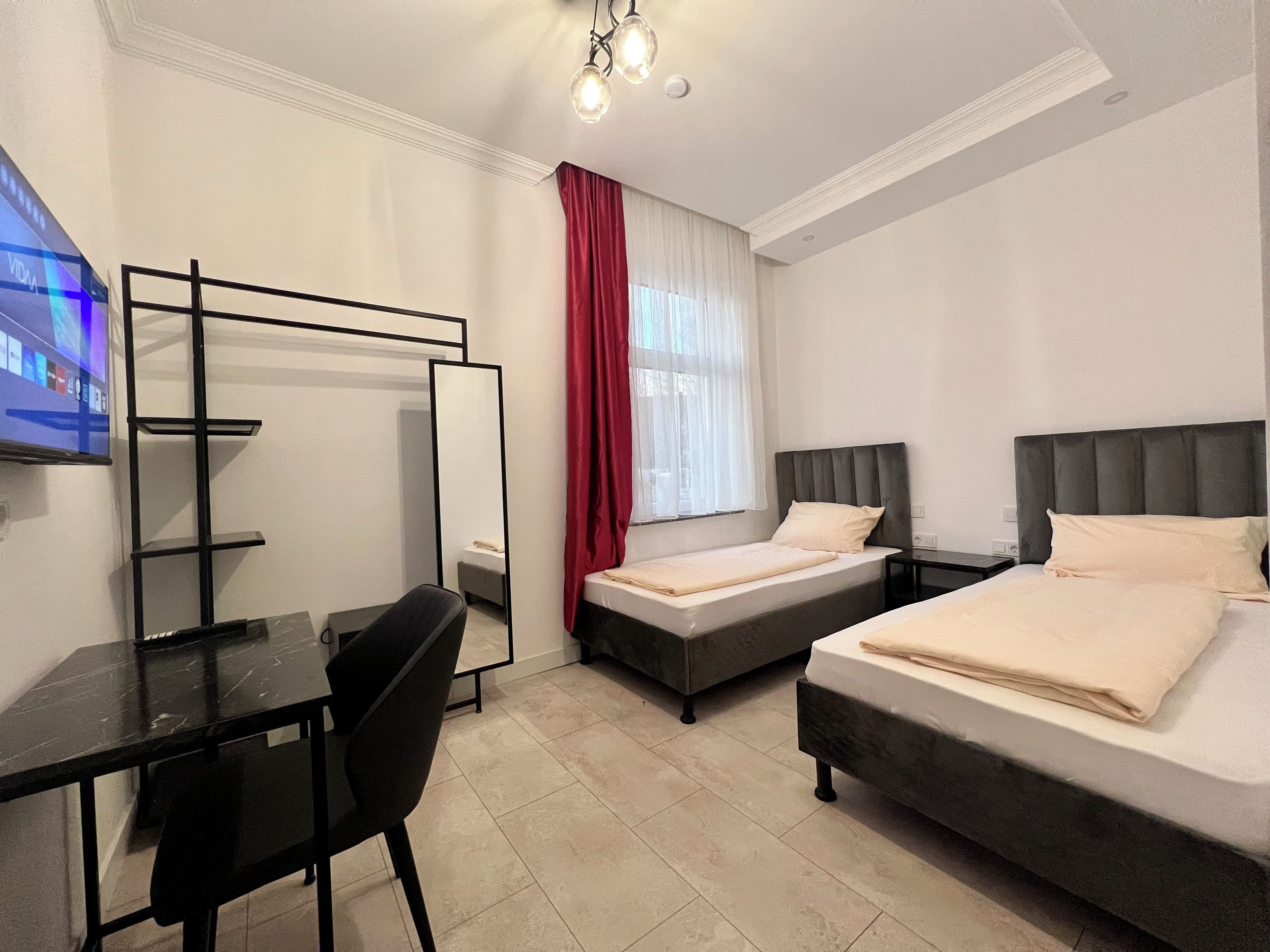 A hotel room with two beds, a desk, a chair, a TV, and a mirror.