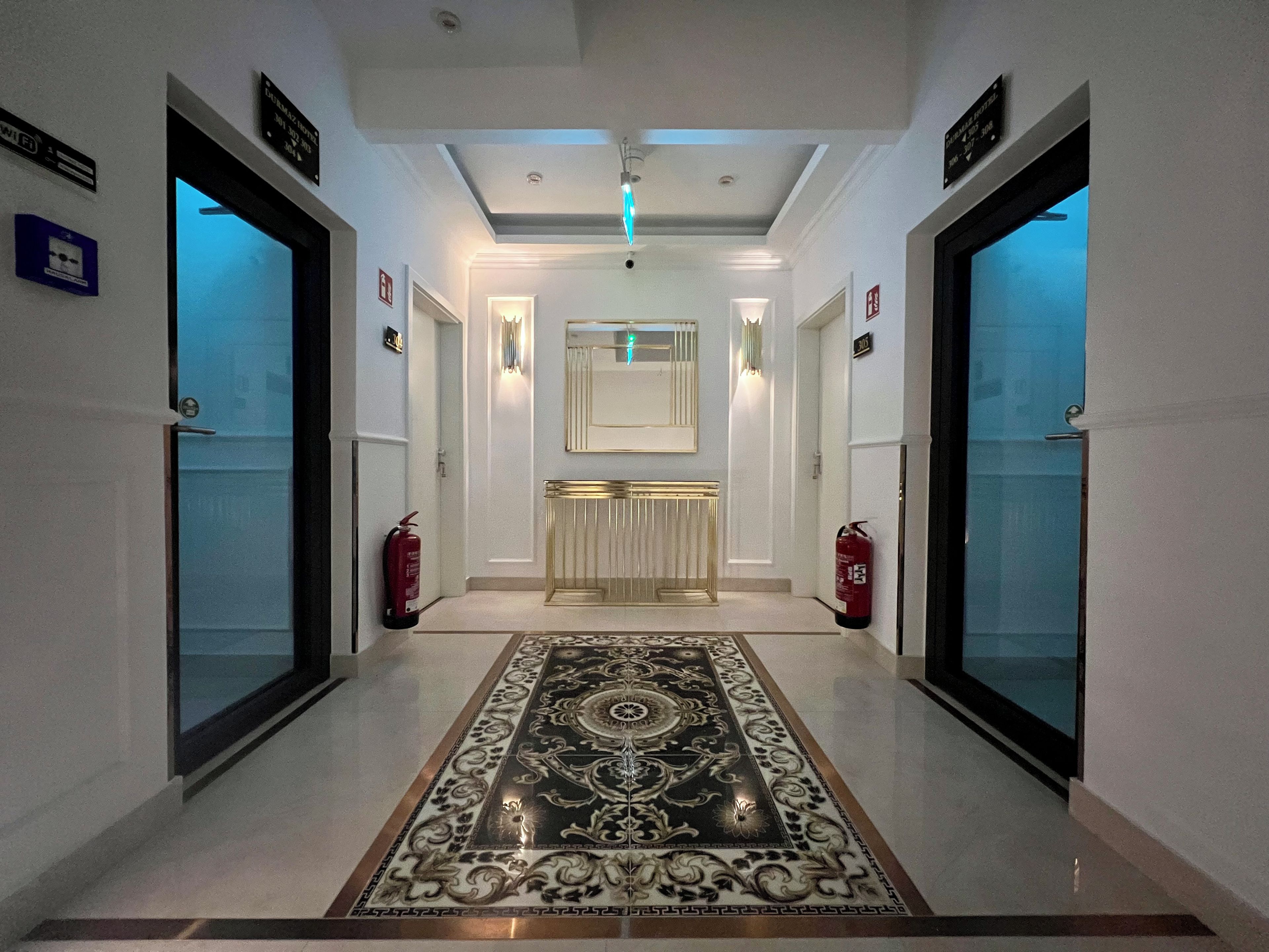 Un pasillo con alfombra estampada, un mostrador de recepción y extintores a ambos lados.
