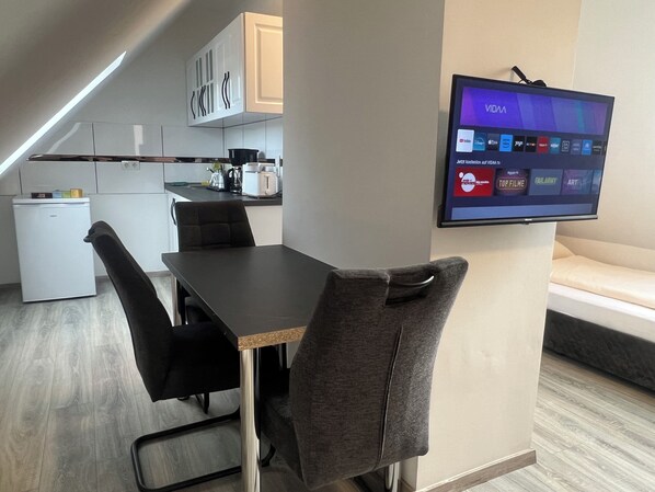 A modern kitchen with a dining area, a flat-screen TV mounted on the wall, and a small refrigerator. - Durmaz Hotel (Hannover)