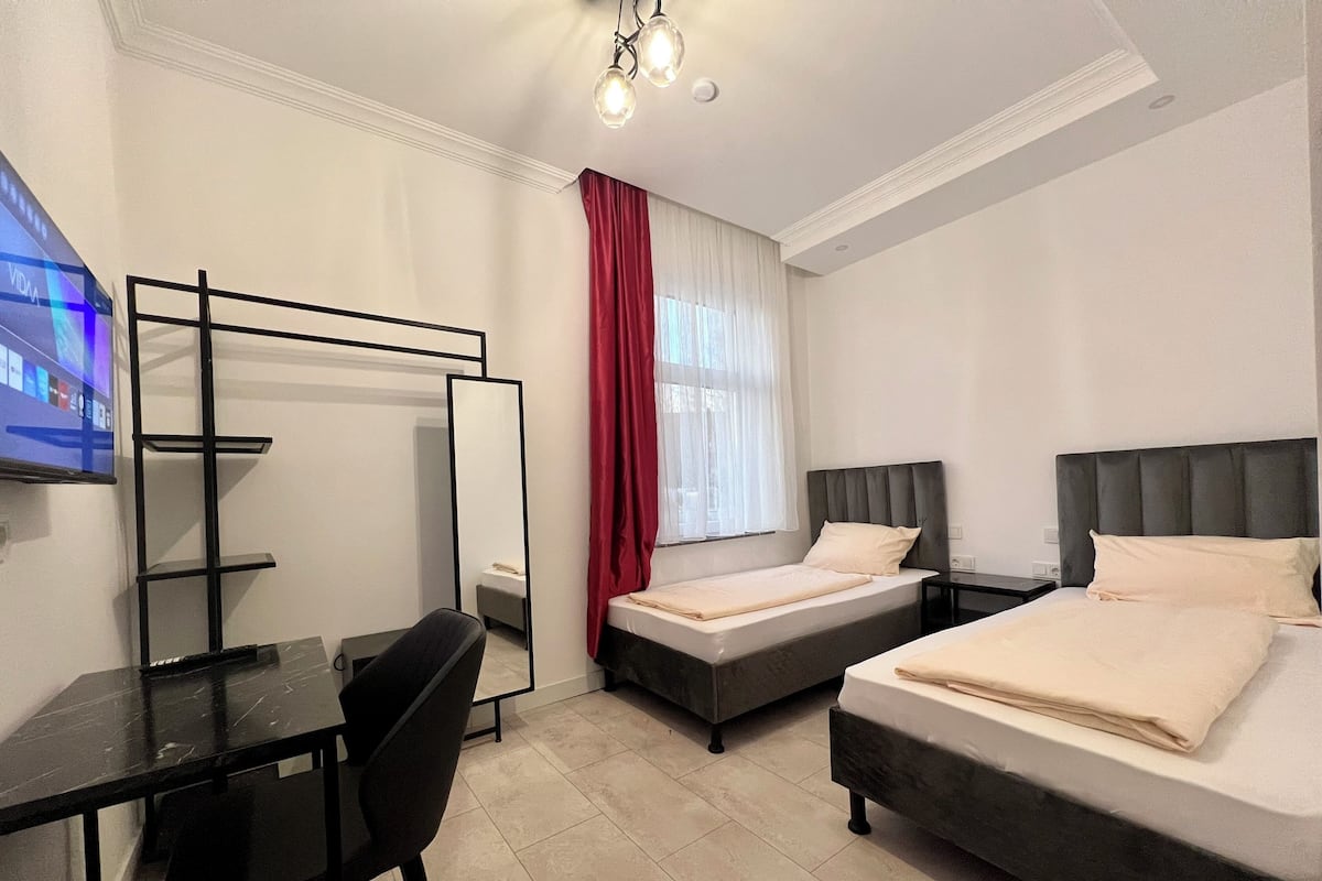 A hotel room with two beds, a desk, a chair, a TV, and a large mirror.