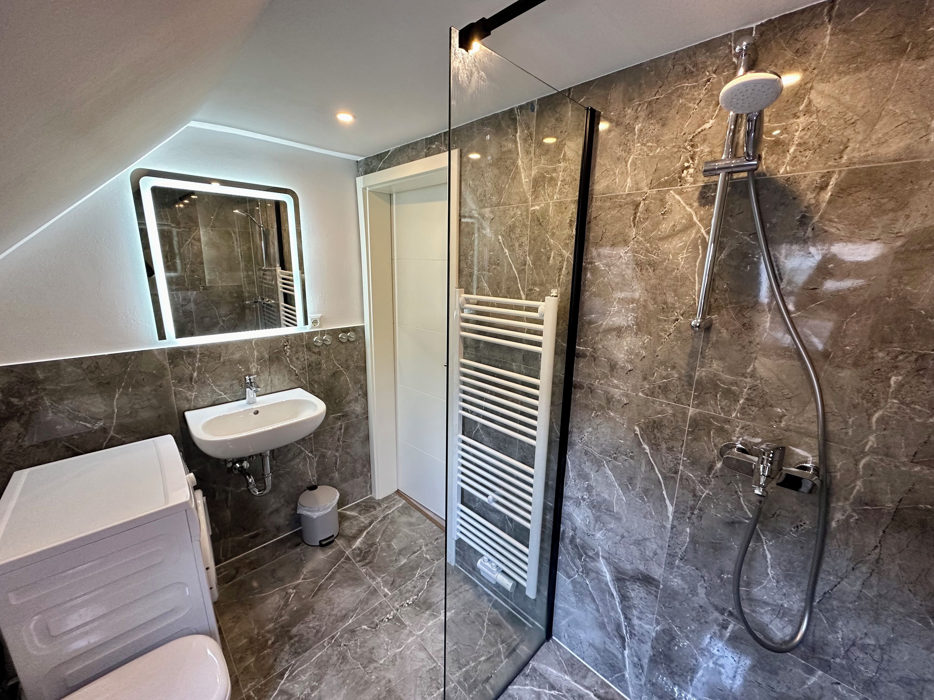 A modern bathroom with a glass shower enclosure, a white sink, and a towel rack.