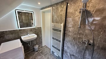 A modern bathroom with a glass shower enclosure, a white sink, and a towel rack.